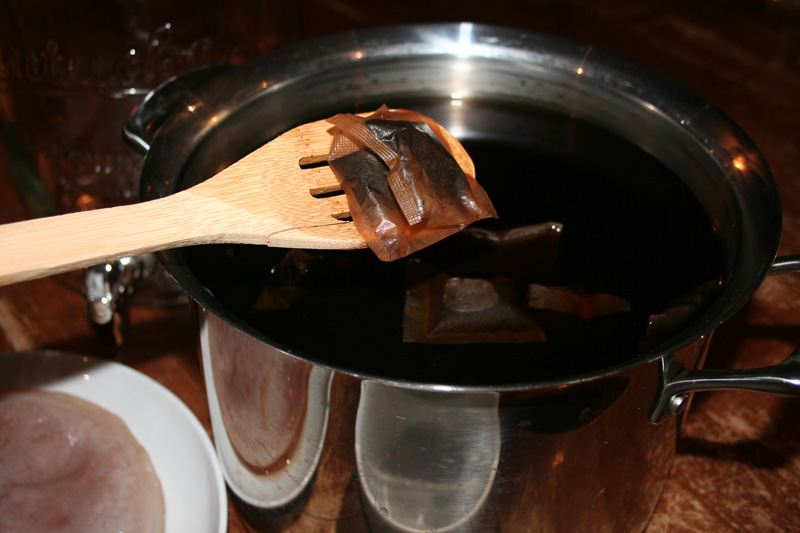 Fishing out tea bags from a large pot of brewed tea for homemade kombucha.