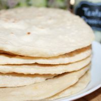 Easy Homemade Sourdough Flatbread stacked on a plate with chicken gyro fixings in the background.