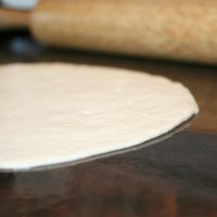 Sourdough Tortilla being rolled thin on a countertop with rolling pin in background.