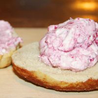 Bagel with raspberry cream cheese on top made from homemade sour cream and cream cheese recipe.