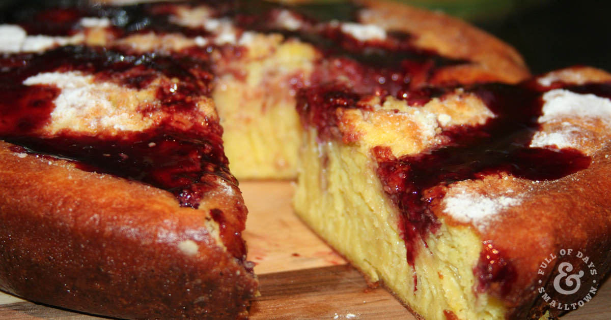 Sourdough Dutch Baby Pancake with a slice cut out, drizzled with marionberry syrup and dusted with powdered sugar.