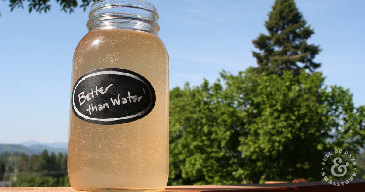 Better Than Water in a quart mason jar, sitting on deck railing with blue sky and green trees in the background.