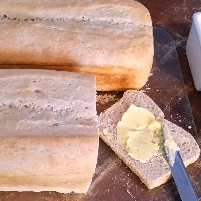 Fresh loaves of homemade sourdough bread, sliced with butter spread on top.