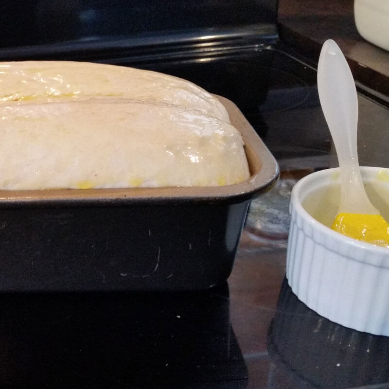 Brushing a risen loaf of homemade sourdough bread with melted butter for better browning during baking.