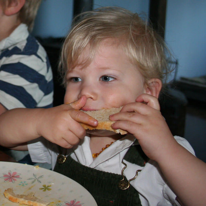 Little boy taking a big bite of a slice of homemade sourdough bread.