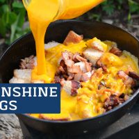 Sunshine Eggs Camping Breakfast, image shows eggs being poured into a cast iron pan with bacon and bread cubes.