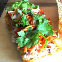 Chicken Banh Mi with pickled radishes and carrots, topped with cilantro and sliced jalapenos on a ciabatta roll.,