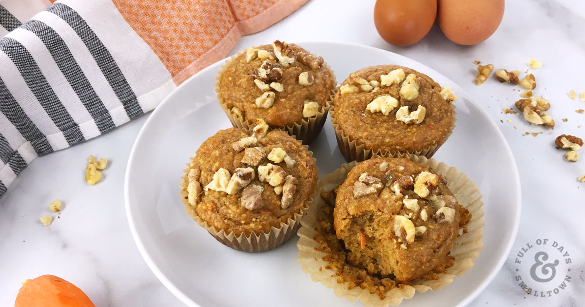 Gluten Free Paleo Carrot Cake Protein Muffins on a plate with eggs, walnuts and carrots in the background.