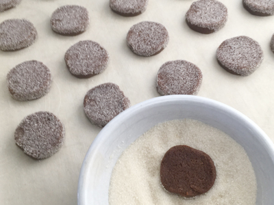 Dipping one side of the chocolate cookie dough into a bowl of organic granulated sugar, then placing on parchment paper before baking.