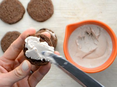 Constructing healthy homemade oreos by spreading chilled coconut cream filling onto a chocolate cookie.