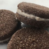 Three homemade Oreo chocolate sandwich cookies stacked on a white countertop.