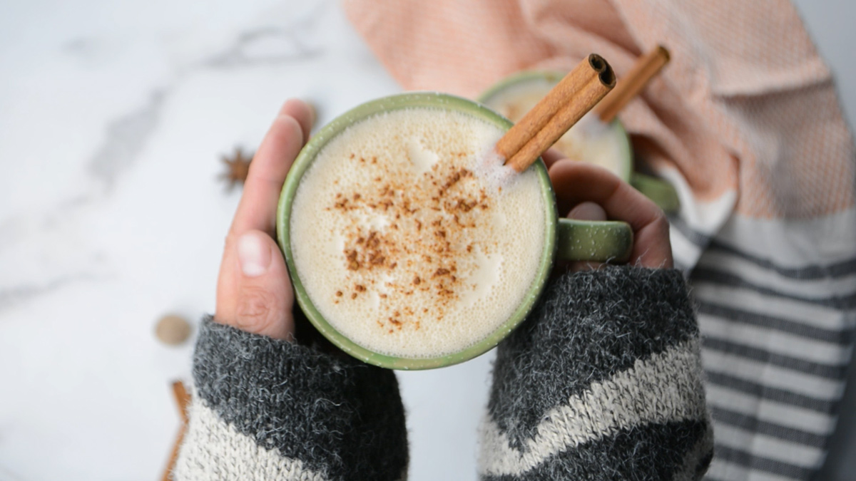 A woman's hands holding a mug of keto chai tea latte with a cinnamon stick in the cup.