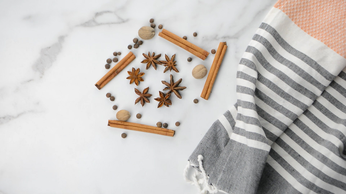 Spices like cinnamon sticks, star anise, peppercorns and nutmeg on a counter.