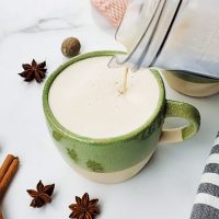 Chai tea latte being poured from a pitcher into mugs.