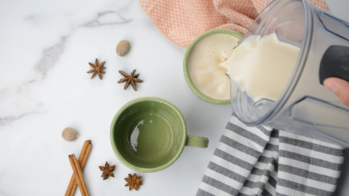 Chai tea latte being poured from a pitcher into mugs.