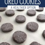 Chocolate sandwich cookies dipped in sugar on a parchment paper lined cookie sheet. Text overlay says, "Homemade Oreo Cookies - A Healthier Option".